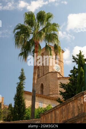 Torre dell'orologio verticale circondata da alberi contro un cielo blu nuvoloso in una giornata di sole Foto Stock