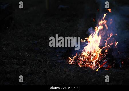 Scintille calde rosse che bruciano volano dal fuoco grande. Carboni brucianti, particelle che fiammano che volano su sfondo nero. Foto Stock