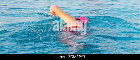 Foto orizzontale di una femmina di nuoto in una piscina al piano terra in prima mattina con un cappuccio rosa. Foto Stock