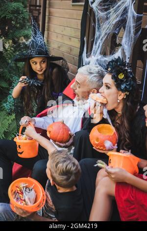 donna che mangia zucca cruda vicino alla famiglia in creepy halloween costumi Foto Stock