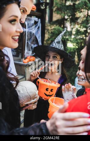 i capretti felici nei costumi di halloween spooky che mangiano le caramelle vicino ai genitori blurred Foto Stock