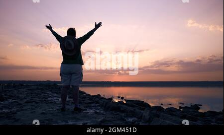Il tramonto e la figura di una donna con le braccia distese e le nuvole si riflettono nell'acqua. Odessa Ucraina, estuario Kuyalnik Foto Stock