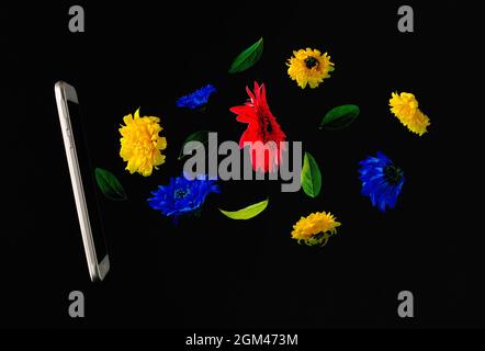 Telefono cellulare con fiori colorati che volano su sfondo nero. Economia, pil e crescita delle vendite. Idea pubblicitaria. Annuncio banner minimo Foto Stock