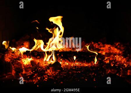Scintille calde rosse che bruciano volano dal fuoco grande. Bel sfondo astratto sul tema del fuoco. Carboni brucianti, particelle infiammate che volano contro la colpa Foto Stock