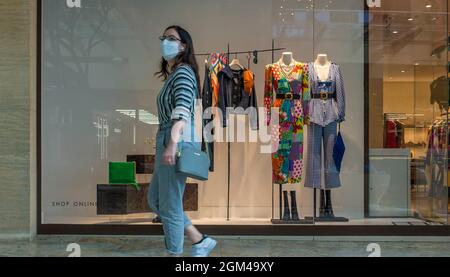 Una giovane donna che indossa una maschera per il viso passa davanti a una finestra di un negozio di abbigliamento in un centro commerciale a Città del Messico durante la pandemia di Covid-19 Foto Stock