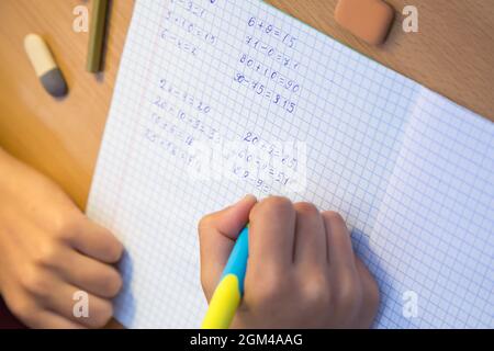 La mano della pupilla ravvicinata risolve gli esempi di matematica in un notebook. Uno scolaro svolge un compito sul posto di lavoro. Il concetto di educazione dei bambini, di insegnamento delle conoscenze, delle competenze e delle abilità. Foto Stock