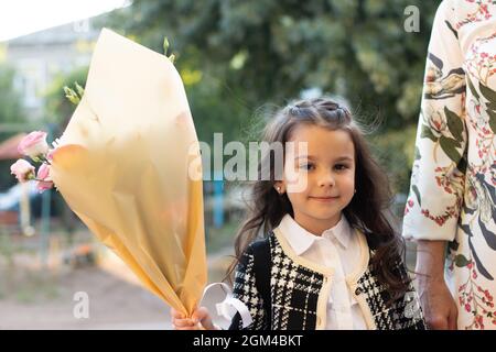 una bambina con capelli lunghi e un bouquet grande nelle sue mani va a scuola per la prima volta. Prima campana a scuola Foto Stock