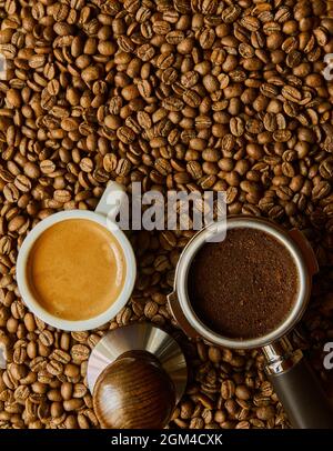 Portafiltro con tavoletta da сoffee, Tempper e tazza espresso sullo sfondo di chicchi di caffè sbriciolati Foto Stock