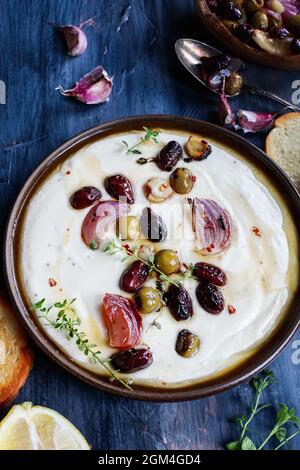 Salsa greca di feta, Tirokafteri, con olive tostate, aglio, cipolle rosse, condito con olio d'oliva e guarnito con timo. Fuoco selettivo su cent Foto Stock