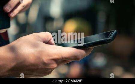 Primo piano della mano utilizzando uno smartphone. Uomo caucasico touch screen telefono cellulare al giorno con il giardino sfondo casa. Navigare in internet, controlla la socia Foto Stock