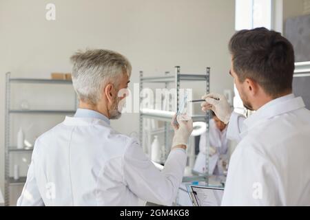 Due scienziati maschi, in piedi con le spalle alla telecamera, guardano una provetta con liquido. Foto Stock