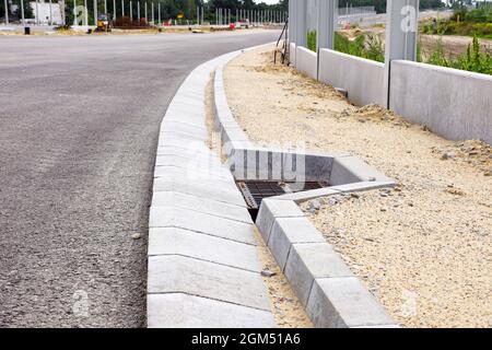 Un sistema di moduli in calcestruzzo per scaricare l'acqua in eccesso dal manto stradale con una griglia di scarico. Costruzione dell'autostrada. Foto Stock