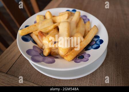Patatine inglesi con formaggio fuso in una ciotola con un disegno floreale su un tavolo di legno. Foto Stock