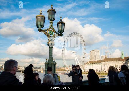 Vista dei turisti dal retro guardando il London Eye in una splendida giornata con cielo blu e grandi nuvole puffy. Foto Stock