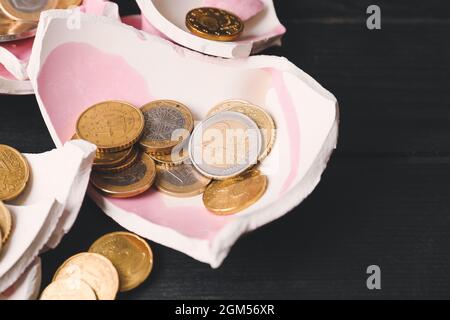 Rottura della banca di maialino con monete su sfondo di legno scuro Foto Stock