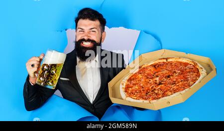 Uomo bearded con pizza saporita e birra guardando attraverso il buco di carta. Gusta una deliziosa pizza e una birra fredda. Foto Stock