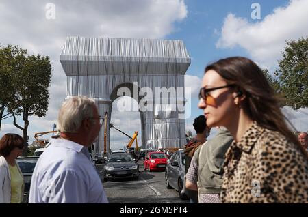 Parigi, Francia. 16 settembre 2021. La gente cammina accanto all'Arco di Trionfo avvolto a Parigi, Francia, il 16 settembre 2021. L'intero Arco di Trionfo in cima agli Champs-Elysees di Parigi è di rimanere avvolto in tessuto per due settimane, un'installazione d'arte concepita dal compianto artista Christo e inaugurata giovedì dal presidente francese Emmanuel Macron. Il monumento alto 50 metri, lungo 45 metri e largo 22 metri costruito da Napoleone, è ora avvolto testa a punta in 25,000 metri quadrati di tessuto argento-blu riciclabile e 3,000 metri di corda rossa. Foto Stock