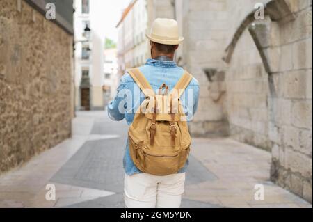 Vista posteriore di un giovane uomo con zaino che cammina sulla strada nella città vecchia. Foto di alta qualità. Foto Stock