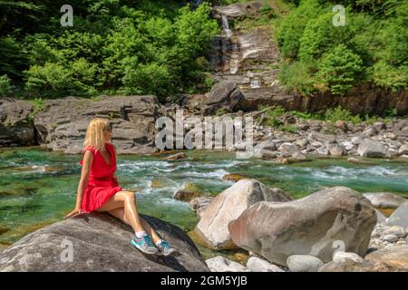 Donna seduta sulle rocce del fiume Verzasca. Valle Verzasca per la città di Lavertezzo. Famoso punto di riferimento per lo svago lungo il fiume e le immersioni in Ticino Foto Stock