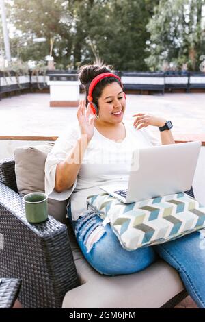 Giovane donna latina curvo con computer che fa videochiamata seduta sulla terrazza in America Latina Foto Stock