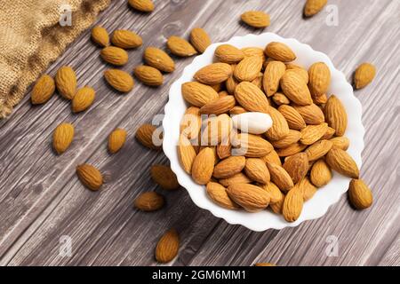 Vista dall'alto delle mandorle in una ciotola bianca su sfondo di legno Foto Stock