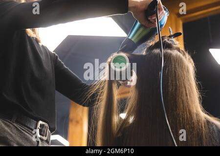 Master donna parrucchiere asciuga i capelli della ragazza con un asciugacapelli e pettini dopo il lavaggio nel salone di bellezza Foto Stock