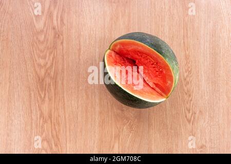 Cocomero senza semi che è stato tagliato un pezzo generoso per rinfrescarsi a proprio agio su un fondo di quercia Foto Stock