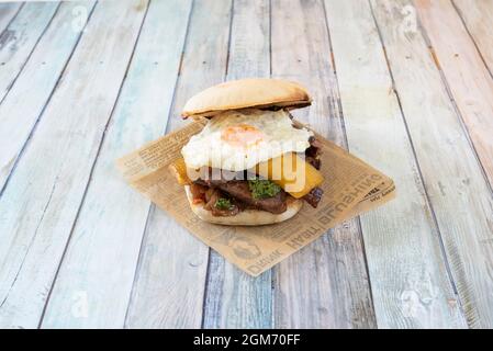 Sanguchon peruviano con filetto di manzo, salsa alle erbe, banana matura fritta e uova fritte su carta di notizie di affari Foto Stock