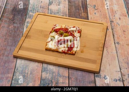 Fetta quadrata di pizza con pomodoro secco, olive, mozzarella, pasta e pomodoro su tavola di legno Foto Stock