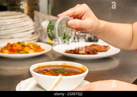Cuocete le mani versando erba cipollina pretagliata in una ciotola di ramen caldo. Foto Stock