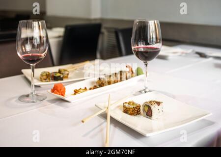 Piatti di uramaki assortiti con bicchieri da vino sul tavolo del ristorante con tovaglie bianche Foto Stock