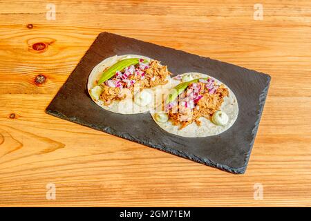 Tacos messicani di cocinita pibil con avocado su piatto di ardesia nera e tavolo in legno Foto Stock