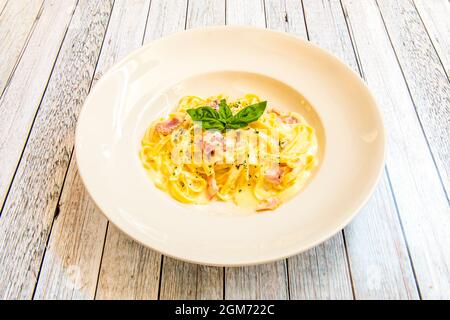 Piatto di tagliatelle con salsa di carbonara e guanciale fritto su un piatto bianco con foglie di basilico Foto Stock