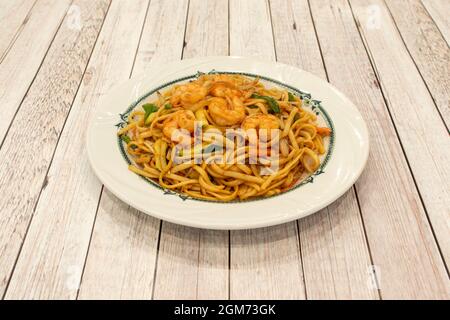 Tagliatelle cotte in un wok in un ristorante cinese con gamberi fritti pelati, zucchine con pelle, cipolla e germogli di fagioli. Foto Stock