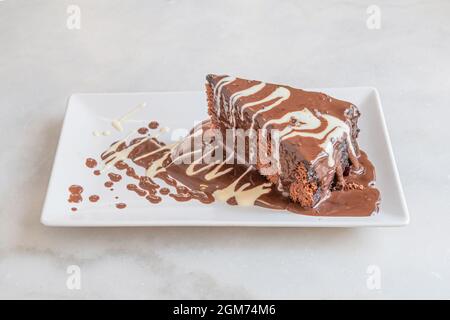 Porzione di torta al cioccolato bagnata con abbondante sciroppo di cioccolato bianco e ancora più sciroppo di cioccolato con latte Foto Stock
