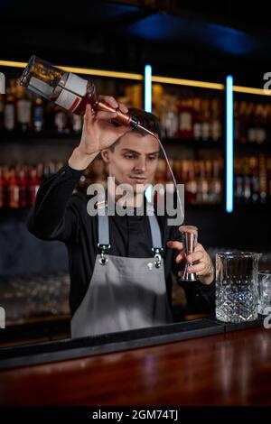 Barman in grembiule aggiunge l'ingrediente al vetro Foto Stock