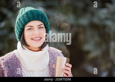 Primo piano ritratto della donna che cammina il giorno d'inverno, tenendo in mano tazza di viaggio in acciaio inox con caffè caldo. Bottiglia d'acqua riutilizzabile. Rifiutare, ridurre, riciclare a. Foto Stock