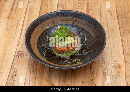 Tartare di tonno rosso piccante su avocado tritato, foglie di germogli di lattuga assortite, germogli di fagiolo all'interno di una bella ciotola nera e ta di legno non verniciato Foto Stock