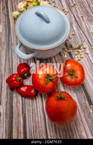 Pentola smaltata in blu cielo e stringa di pomodori maturi su tavola di legno Foto Stock