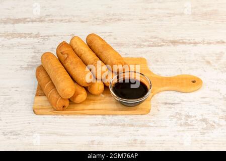 Un mucchio di tequeños appena fatto su una tavola di bambù e con sciroppo di mela per immergere Foto Stock