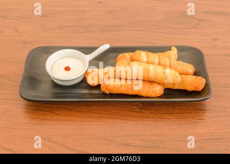 Razione di deliziosi tequeños ripieni di formaggio fritto con salsa di maionese su tavola di legno Foto Stock