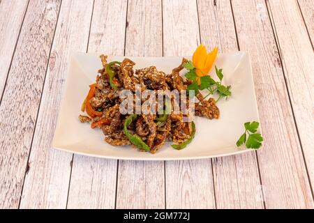 Ricetta cinese con strisce di manzo caramellate fritte con peperoni rossi e verdi fritti e semi di sesamo con cipolla su un piatto bianco Foto Stock