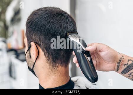 Barbiere taglio dei capelli della nuca di un uomo con una macchina in un salone Foto Stock