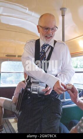 Oggi (2021) ricreazione di un direttore d'autobus degli anni '60 che consegna i biglietti a persone su una macchina d'autobus d'epoca, Epping-Ongar Railway, Essex UK Foto Stock