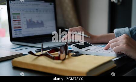 Primo piano mano donna che fa finanza e calcolare con calcolatrice su scrivania circa costo , lavoro da casa concetto Foto Stock