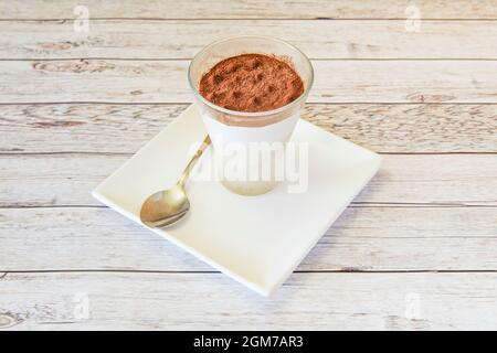 Dessert italiano tiramisù fatto in casa servito in un bel vetro di cristallo cosparso di cacao e un cucchiaio da mangiare Foto Stock