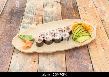 Porzione di tonno maki con riso bianco, tonno rosso, alghe nori, cetriolo a fette, foglia di wasabi e foglie di ginseng su un vassoio bianco Foto Stock