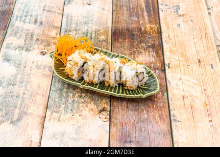 Rotolo di riso Uramaki con cipolla fritta, avocado e pesce farfalla su un piatto verde Foto Stock