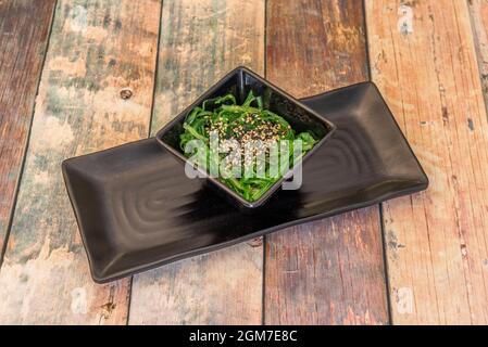 Deliziosa insalata di alghe di wakame con semi di sesamo e papavero in grande quantità all'interno di una ciotola nera e piatto nero Foto Stock