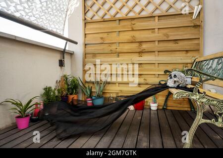 Area giardino su una terrazza urbana con una sedia in ferro, traliccio in legno, diverse piante e un visitatore inaspettato. Cranio messicano Foto Stock